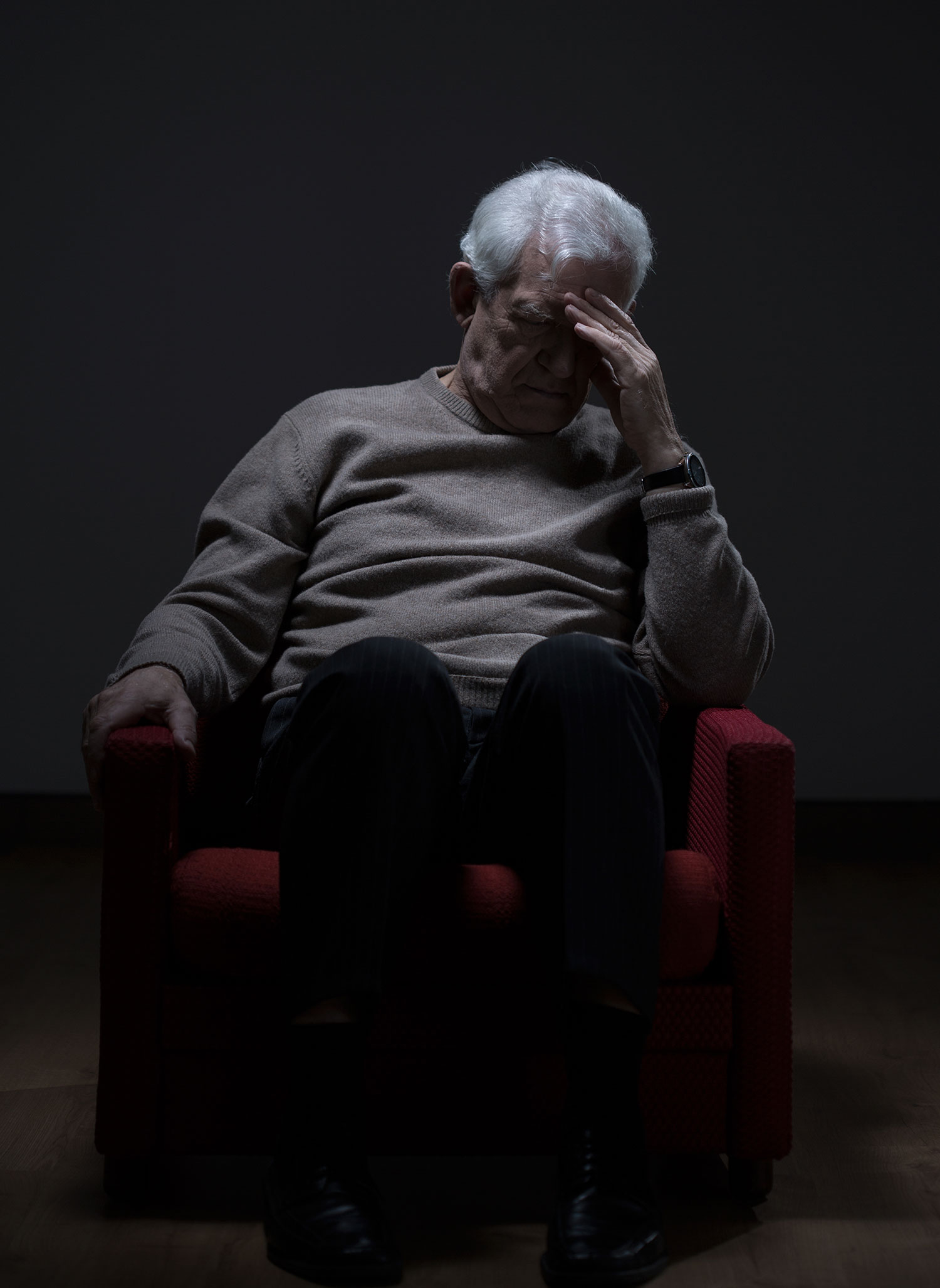 Alter Mann auf rotem Stuhl in dunklem Raum